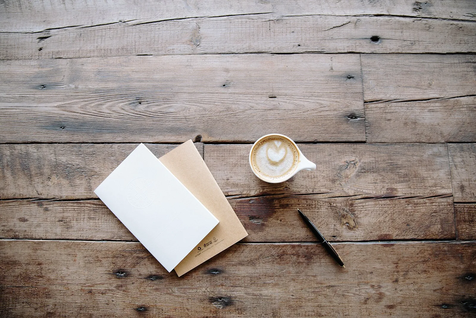 A latte beside a notebook and pen on a wooden table